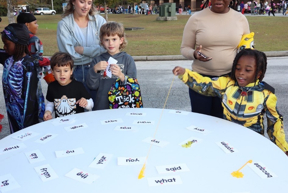 Halloween dressed up students, 3 of them, around a table using sticky hands to grab words.