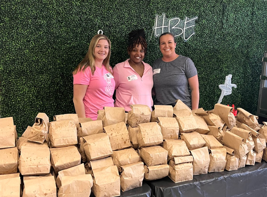 Three volunteers standing behind a table full of brown bags filled with popcorn, ready for delivery.