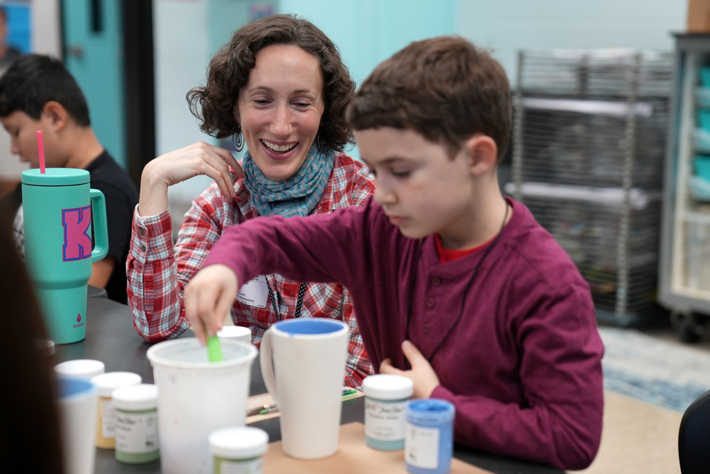 parent smiling while student paints mug