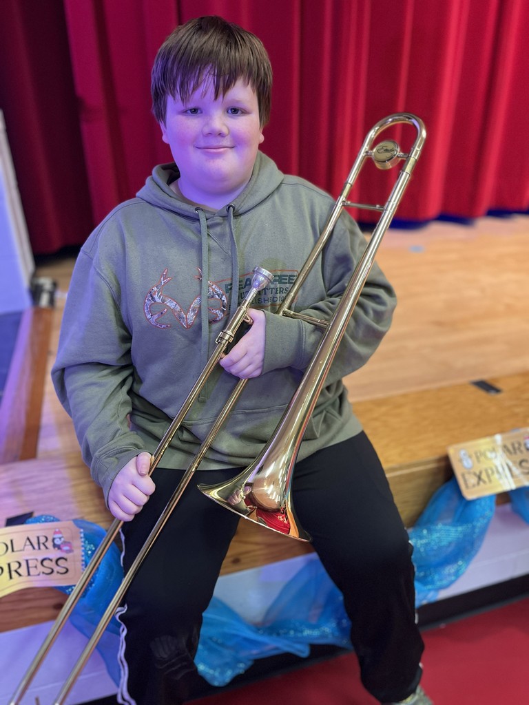 Student holding Trombone sitting on the edge of the stage.