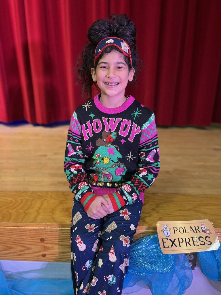 Student wearing and Ugly Sweater, smiling sitting on the edge of the stage.