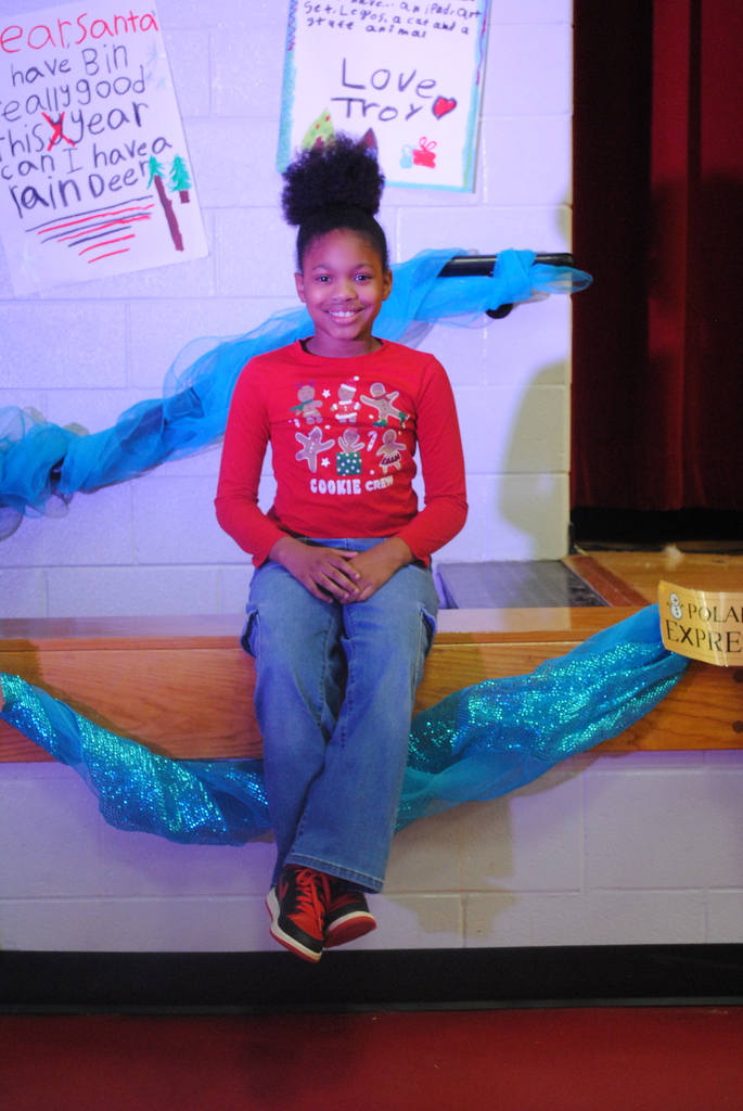 Student sitting on the edge of the stage wearing red shirt and smiling. 