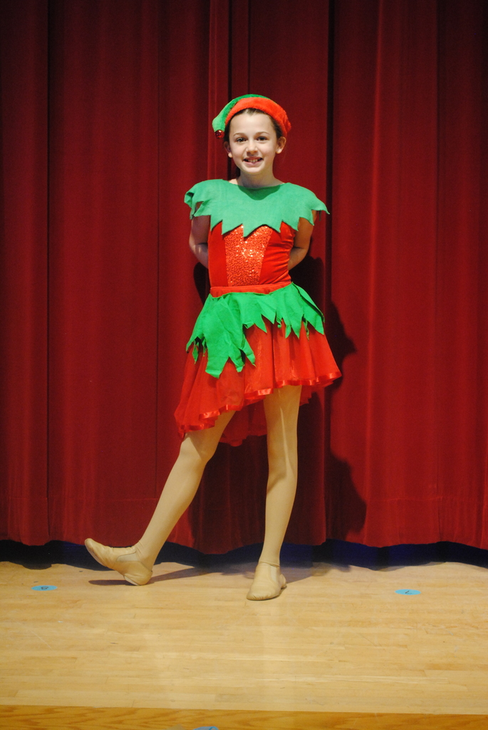 Student wearing red and green costume in front of red curtain. 