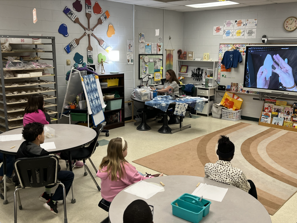 Third grade students in the art room working with artist Cat Brantley. Students are watching a demonstration on indigo dyieing. 