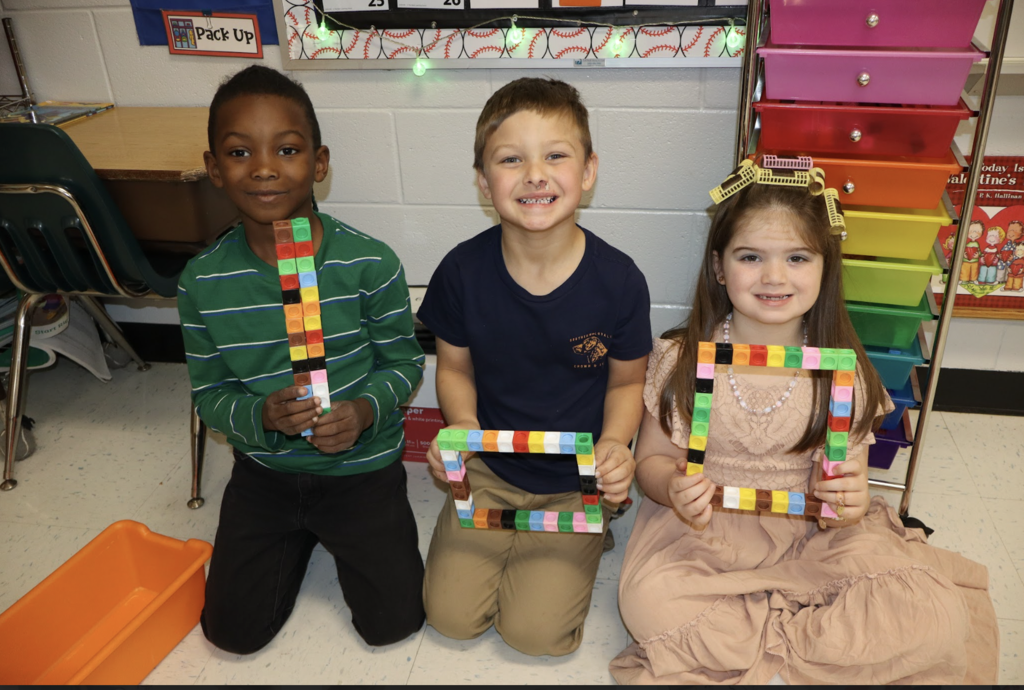 Image of three students holding multicolored cubes to create the number 100! 