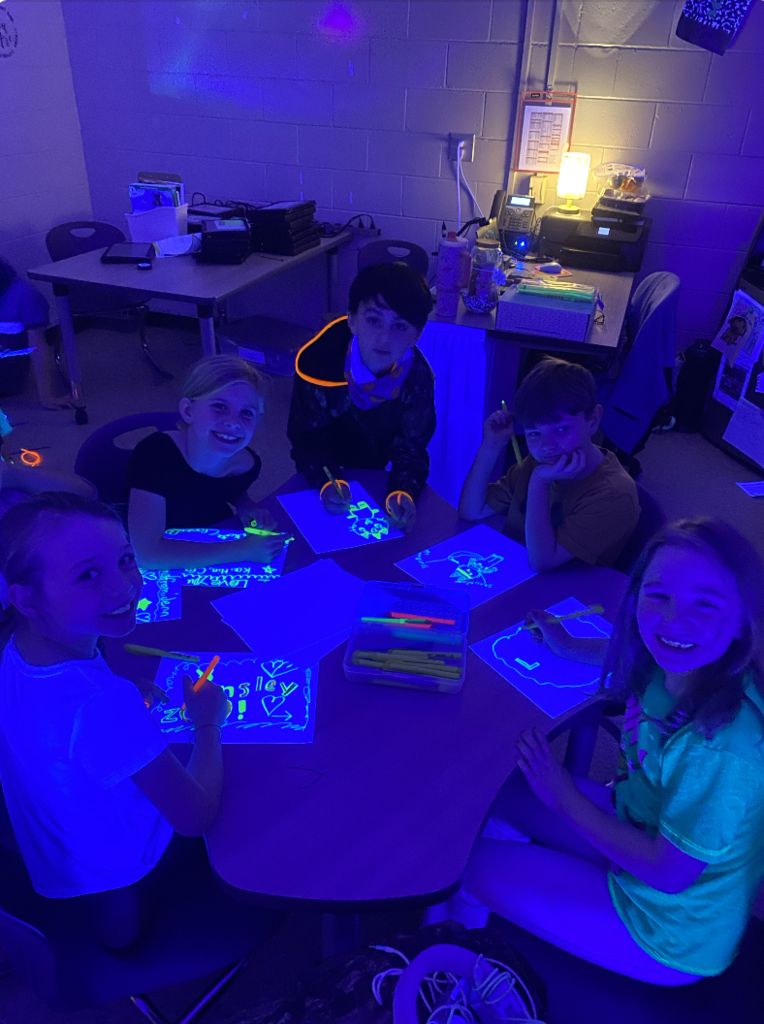 4 students sitting at a desk working on glow in the dark artwork