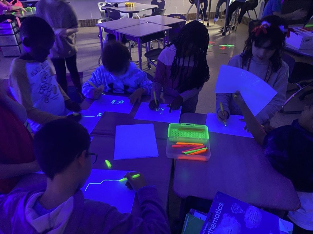 Students standing around a table working with glow in the dark materials 
