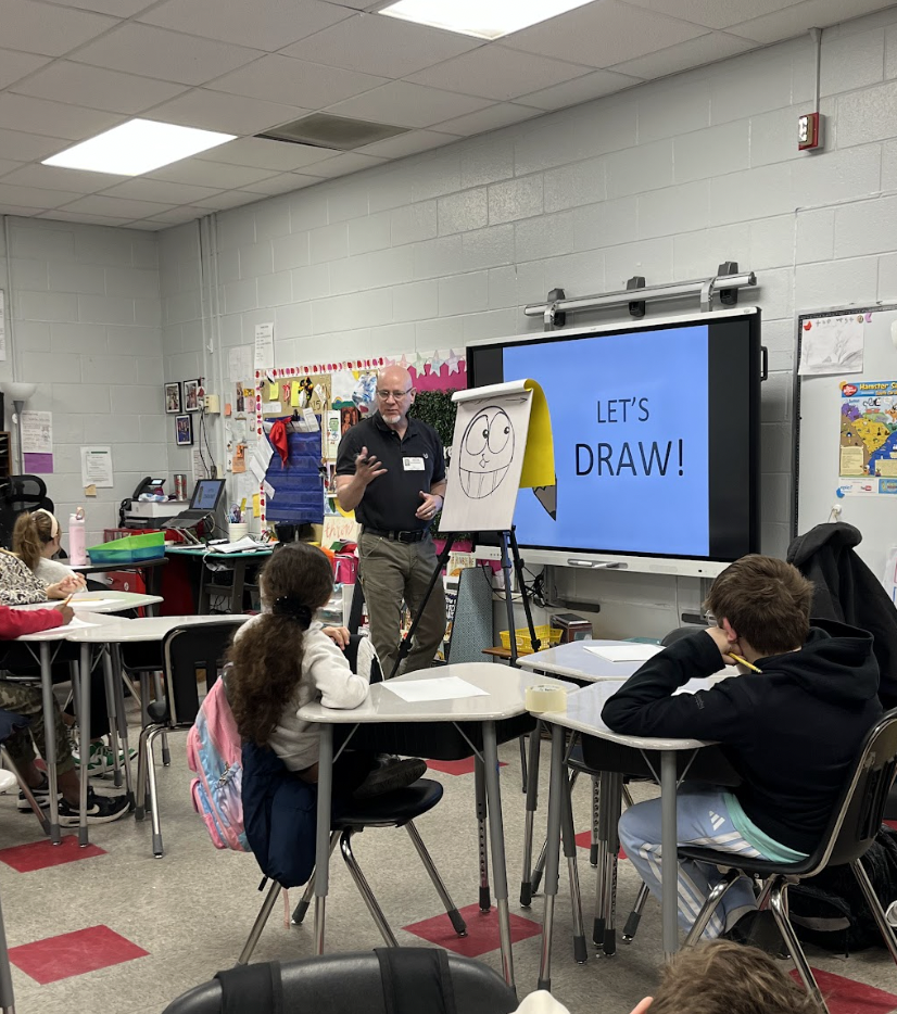 Artist in residence, Dave McDonald standing in front of an easel demonstrating how to draw cartoon characters