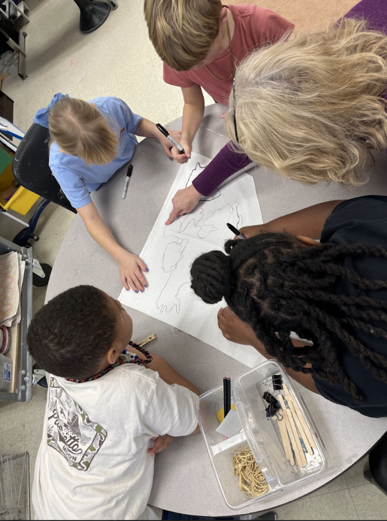 4 students and one teacher working together on drawing their continent for their project. 