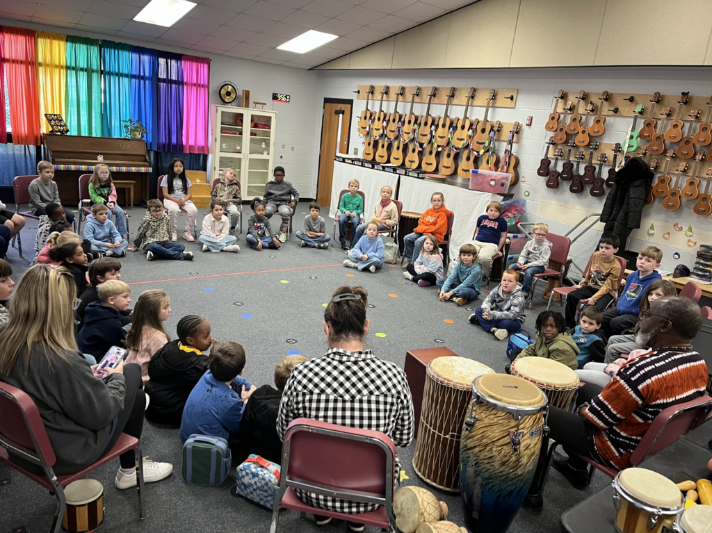 Students sitting in a circle, surrounded by drums! 