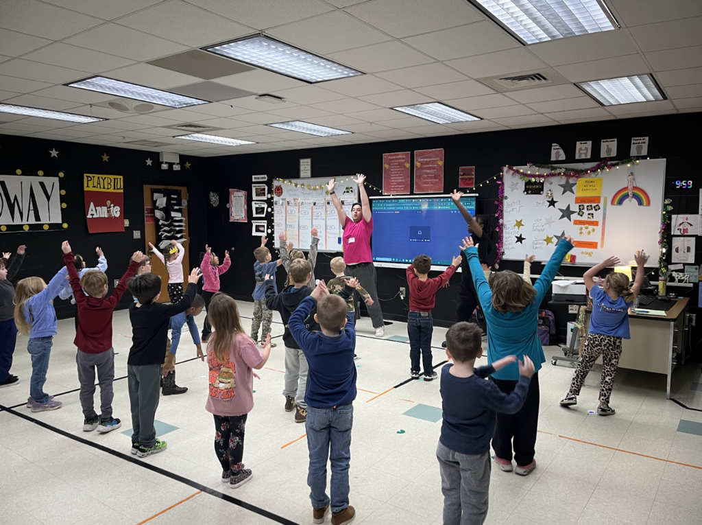 K5 students standing in the drama room, arms reached over head! Dancing with the artist in residence! 