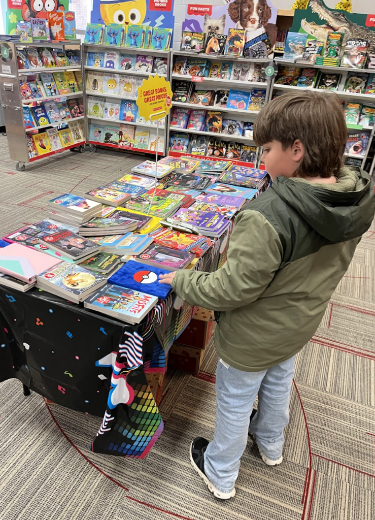 Student standing at a table looking at books in the book fair. 