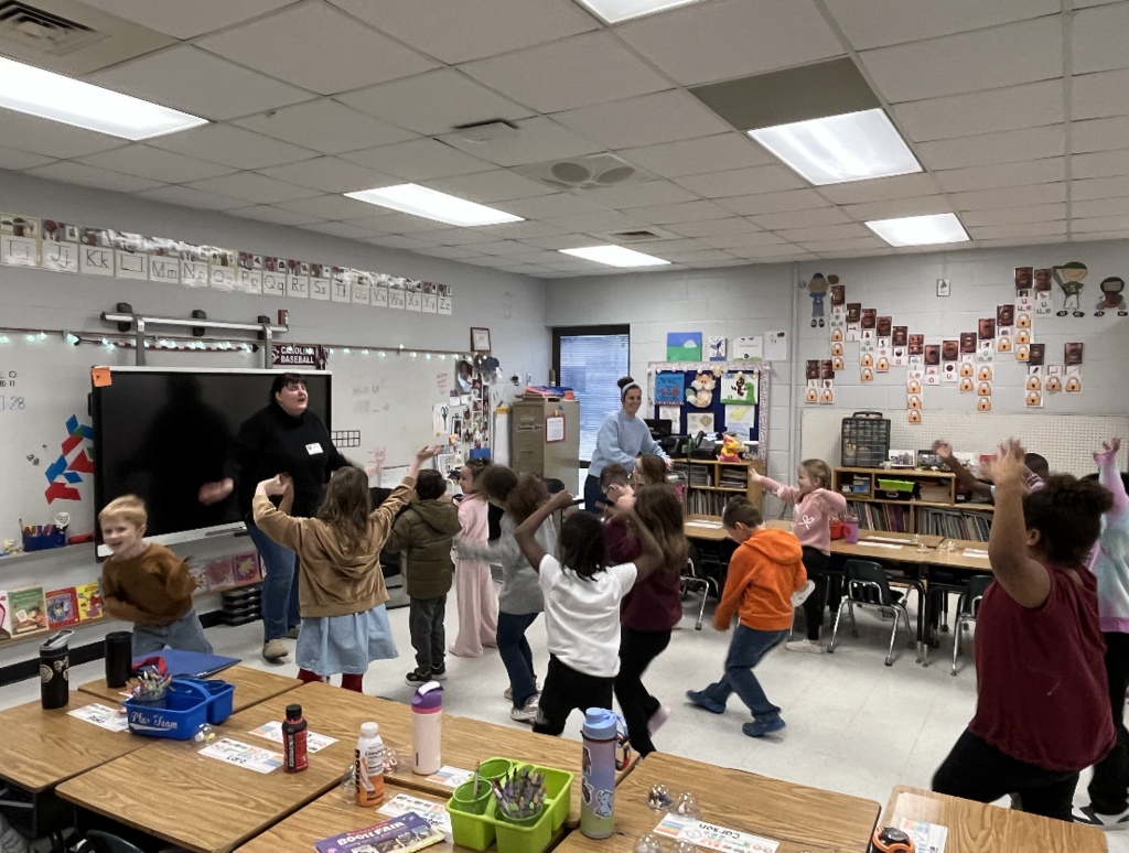 Students standing in classroom moving their arms above their head