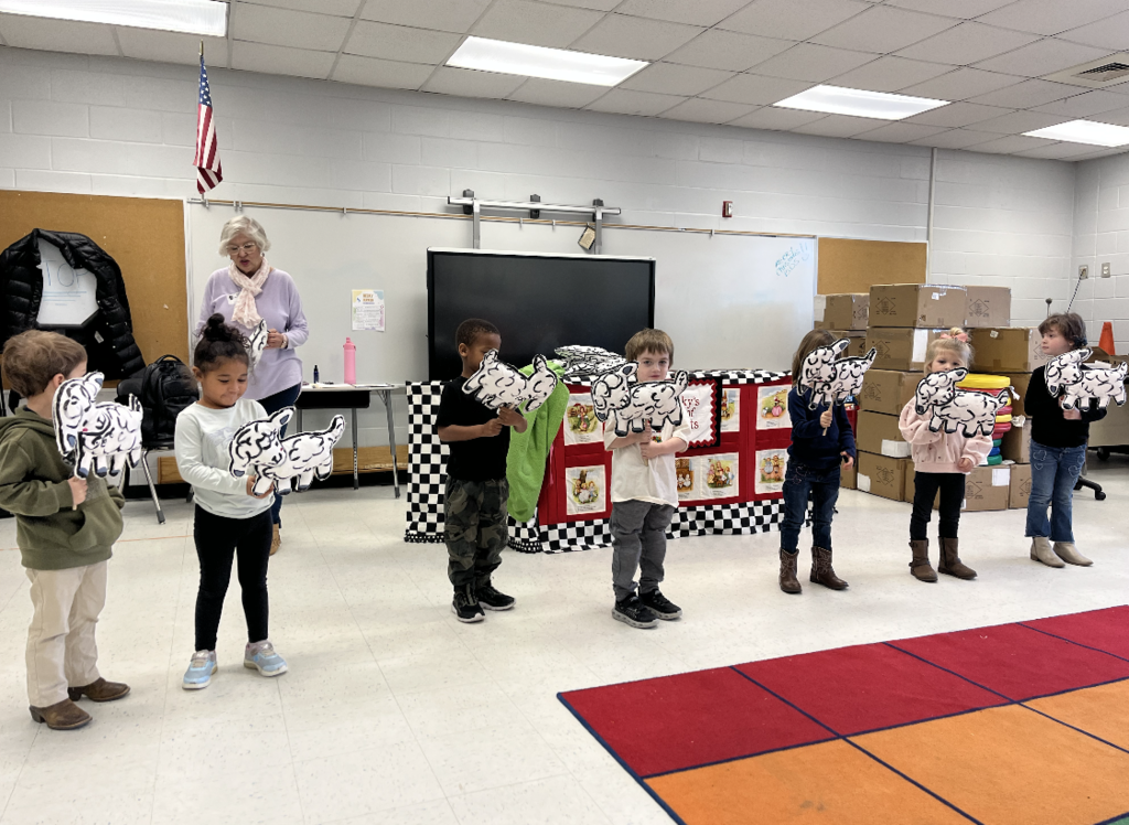 Prekindergarten students holding lamb puppets in the front of the room