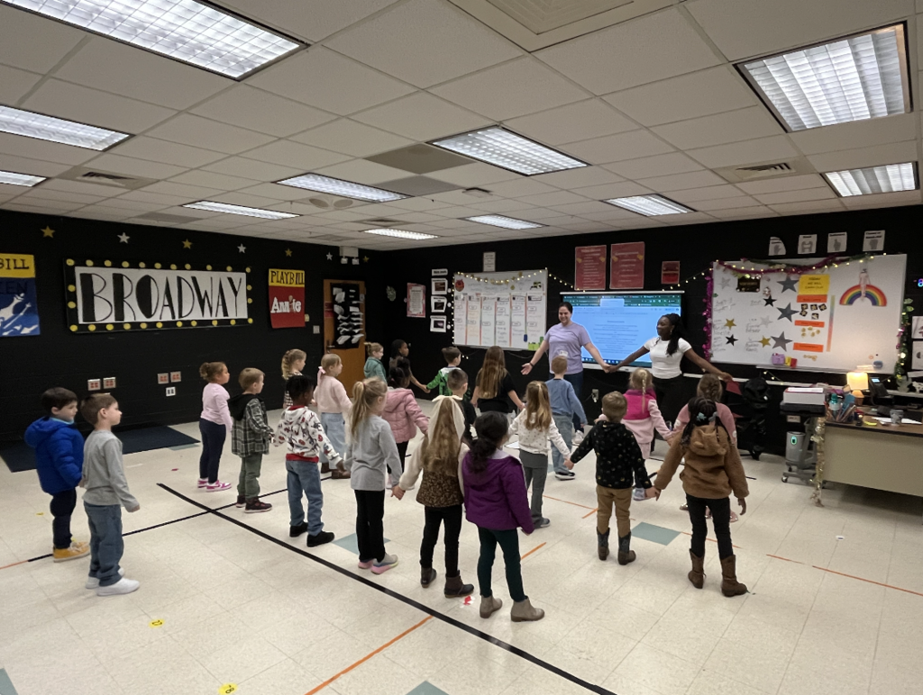 K5 students standing with arms out to the side two residents from the Charleston Stage leading them in warm up