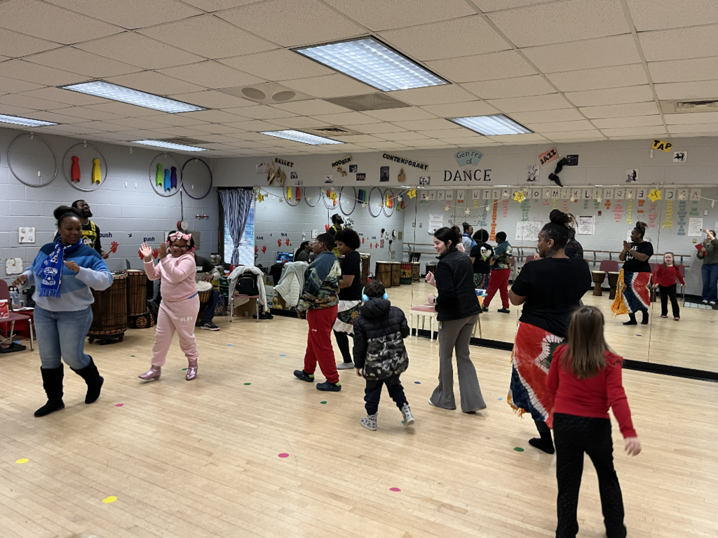 Students walking around in a circle in our dance room, a mirror is behind the students and drums off to the side 