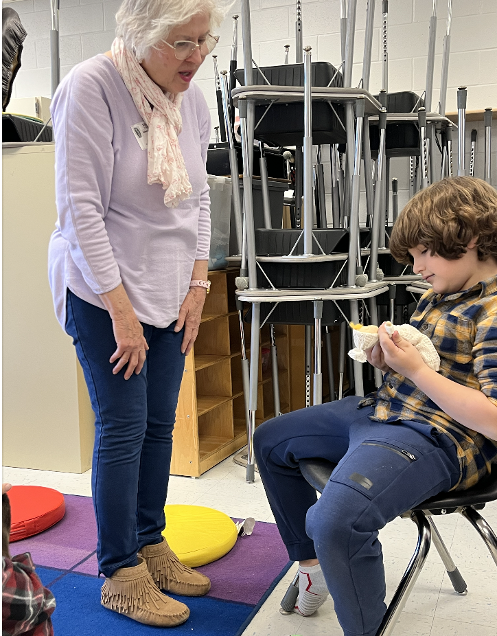 Student is holding a puppet while teacher instructs hi m how to move the arms 