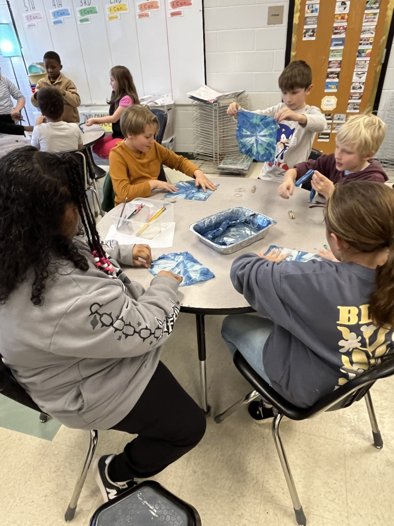 5 students sitting at a table unrolling their indigo dye cloth 