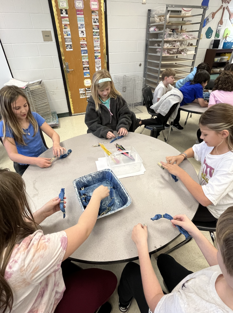 5 students sitting at a table unwraping their indigo dyed cloth