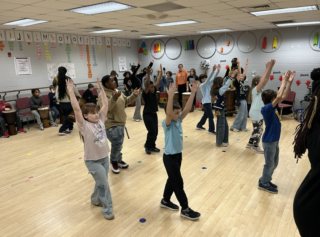 Students standing in the dance room with arms extended over head 