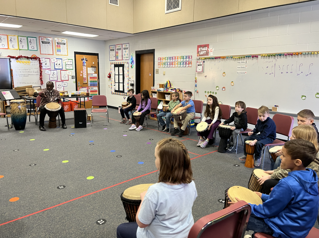 Students sitting on chairs with djembes in front of them playing drums! 