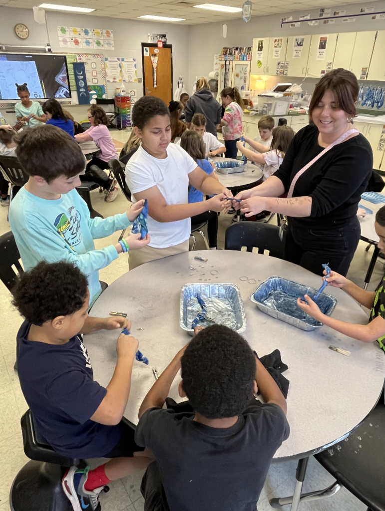 5 students sitting at a table and one teacher unwrapping their cloth that was indigo dyed 