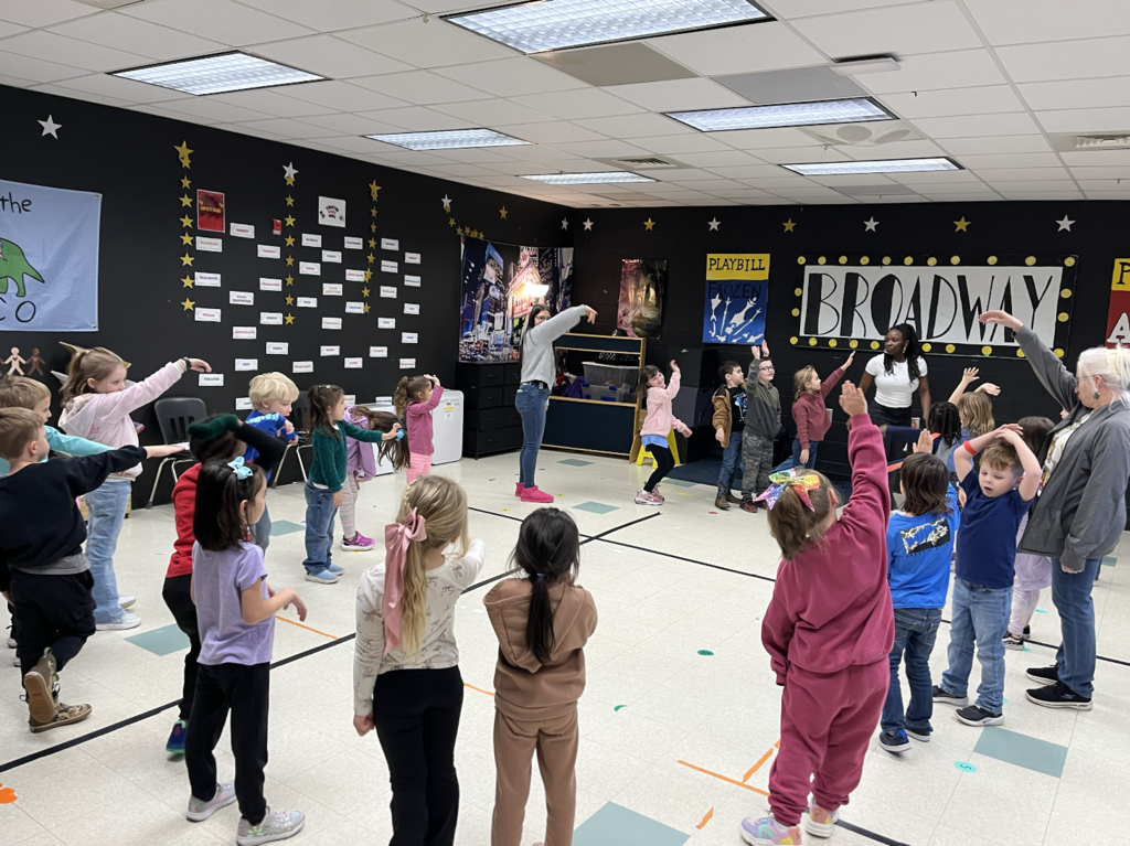 Students are walking around the drama room with arms over head making the shape of an elephant. 