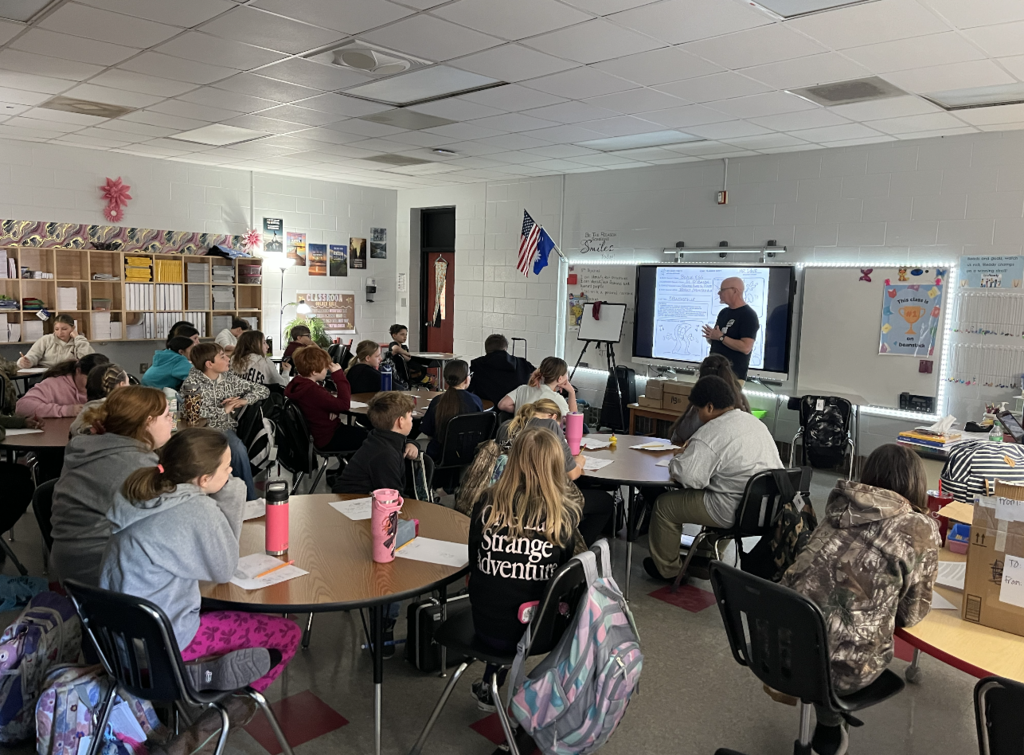 Students sitting at their desks looking at their artist in residence giving instructions on how to create a comic. 