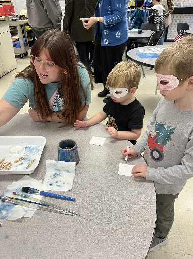 Two young boys wearing masks working with the art teacher 