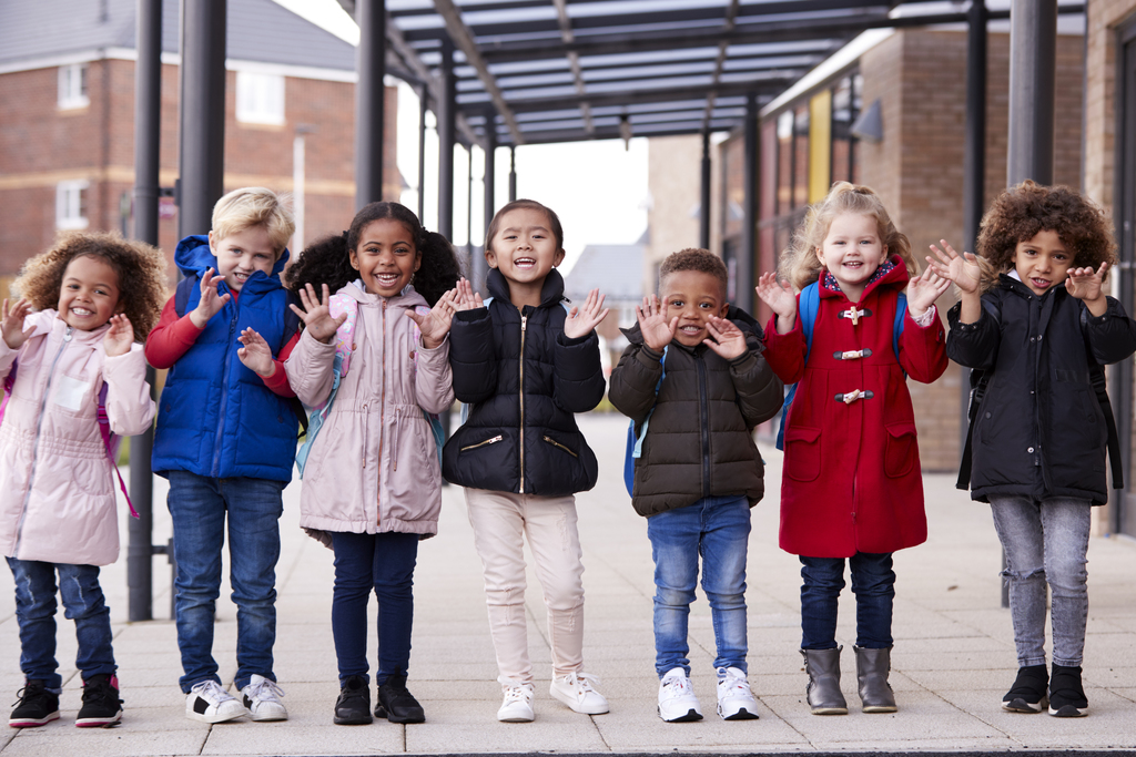 a group of smiling young multi-ethnic school kids waving
