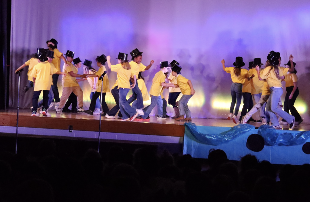 Multiple students wearing yellow shirts and top hats performing on stage 