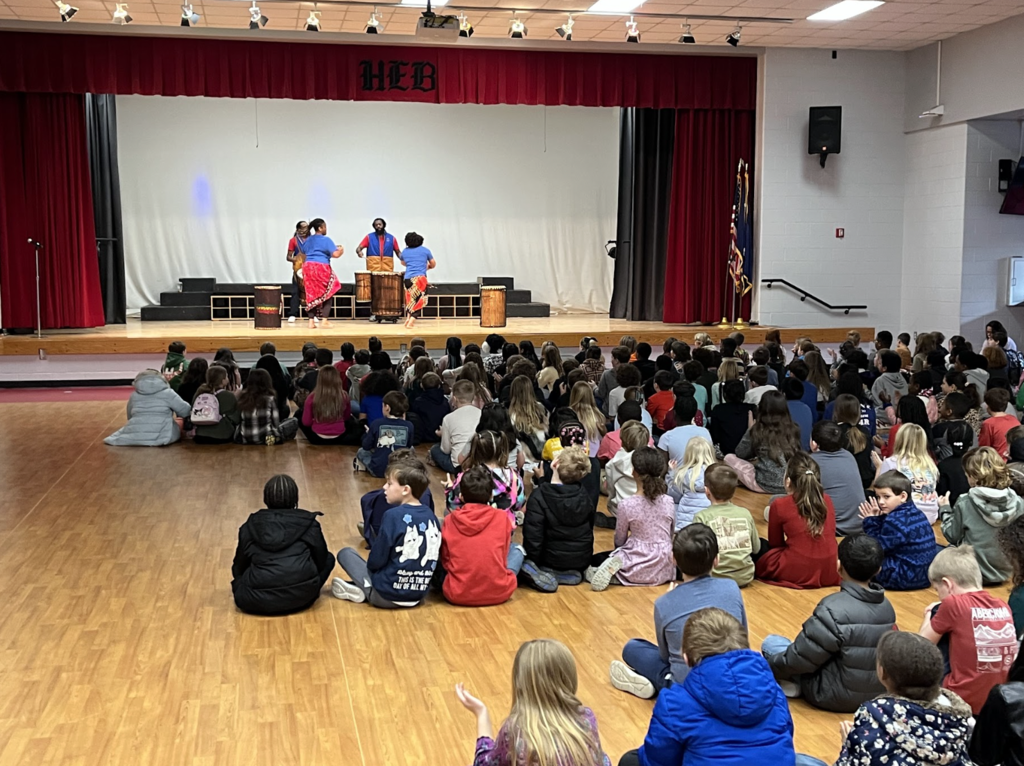 Students sitting in the MPR watching 4 performers on the stage 