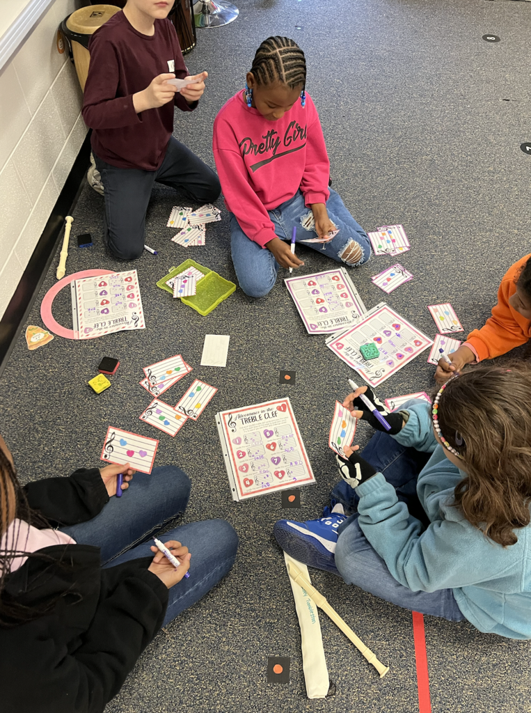 This picture show 5 students sitting on the ground working together on in their recorder center.