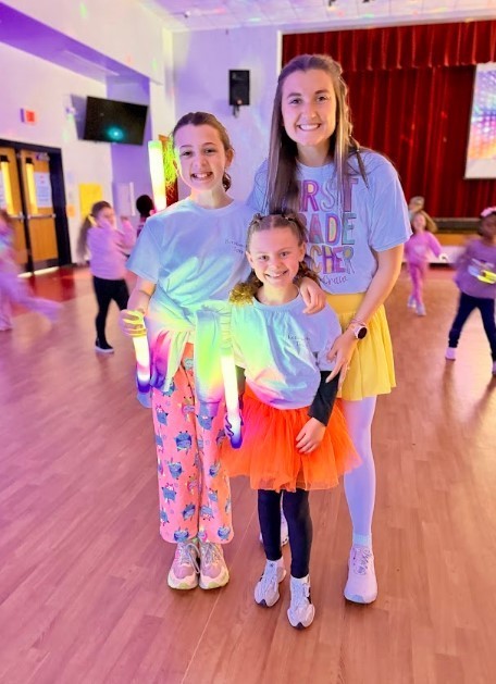 Two girls and teacher wearing bright colors stand together to smile.