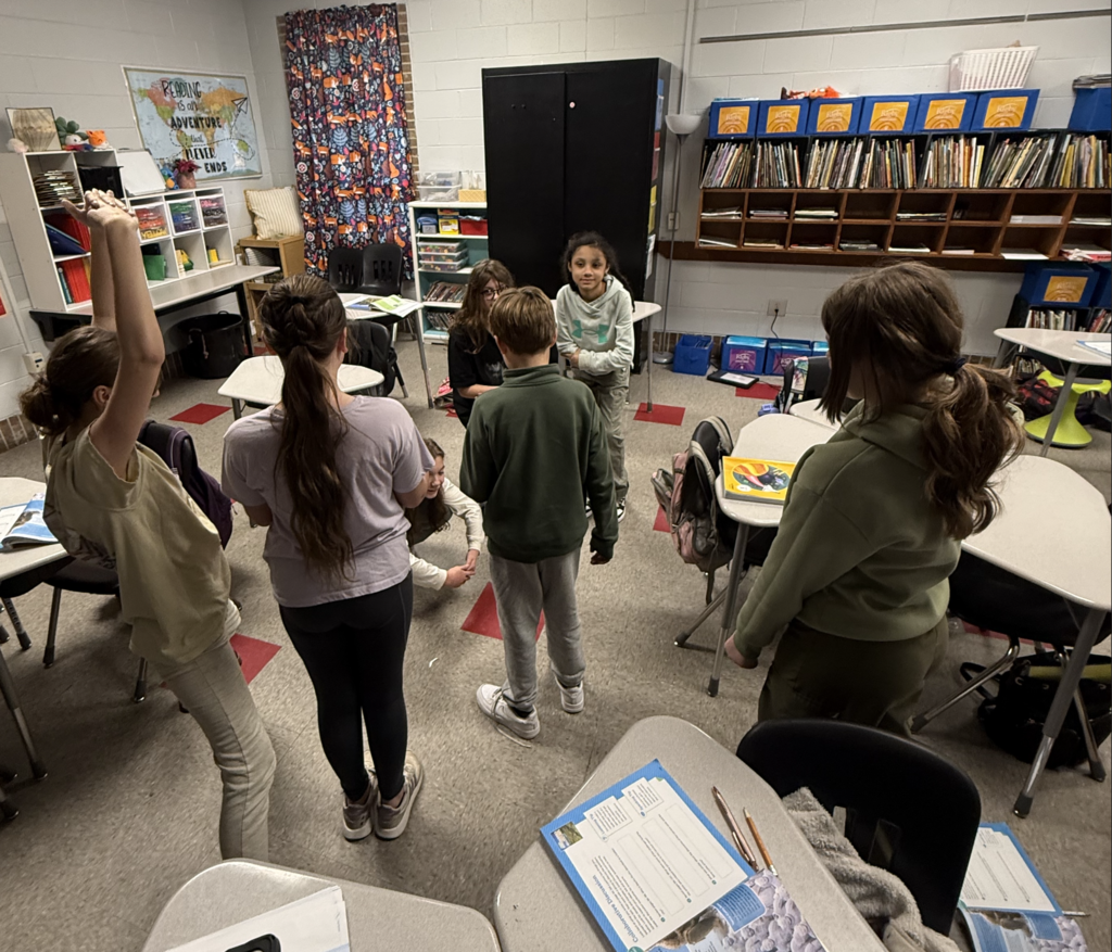 6 students standing at various levels in their classroom working to create. tableau of their story