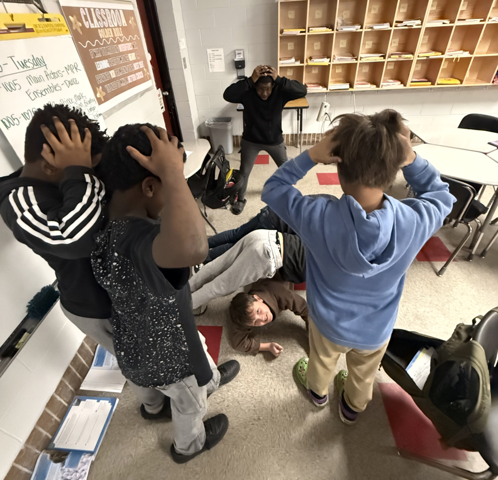 Students with hands on head and two other studnets on the ground creating a tableau summarizing their story