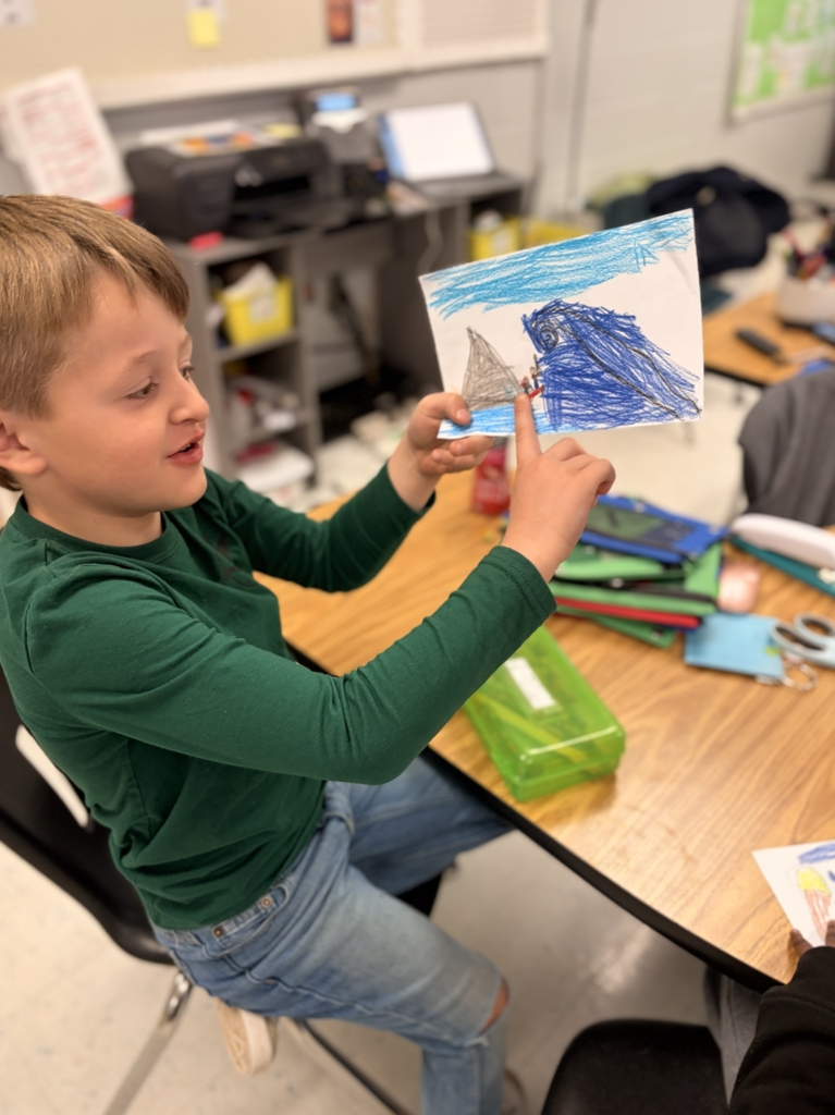 Student pointing to their illustration showing their teacher