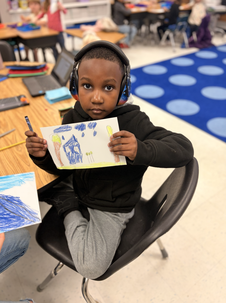 Student holding their illustration seated in a chair