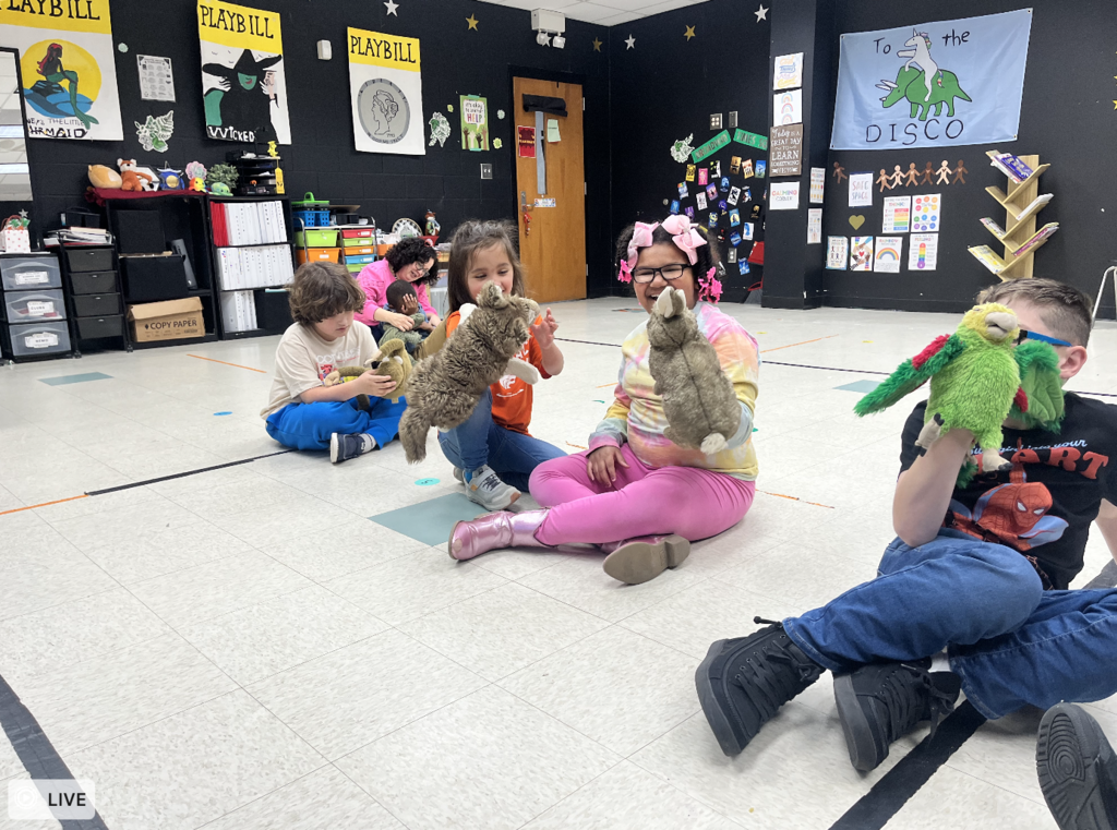 4 students sitting on the ground playing with puppets