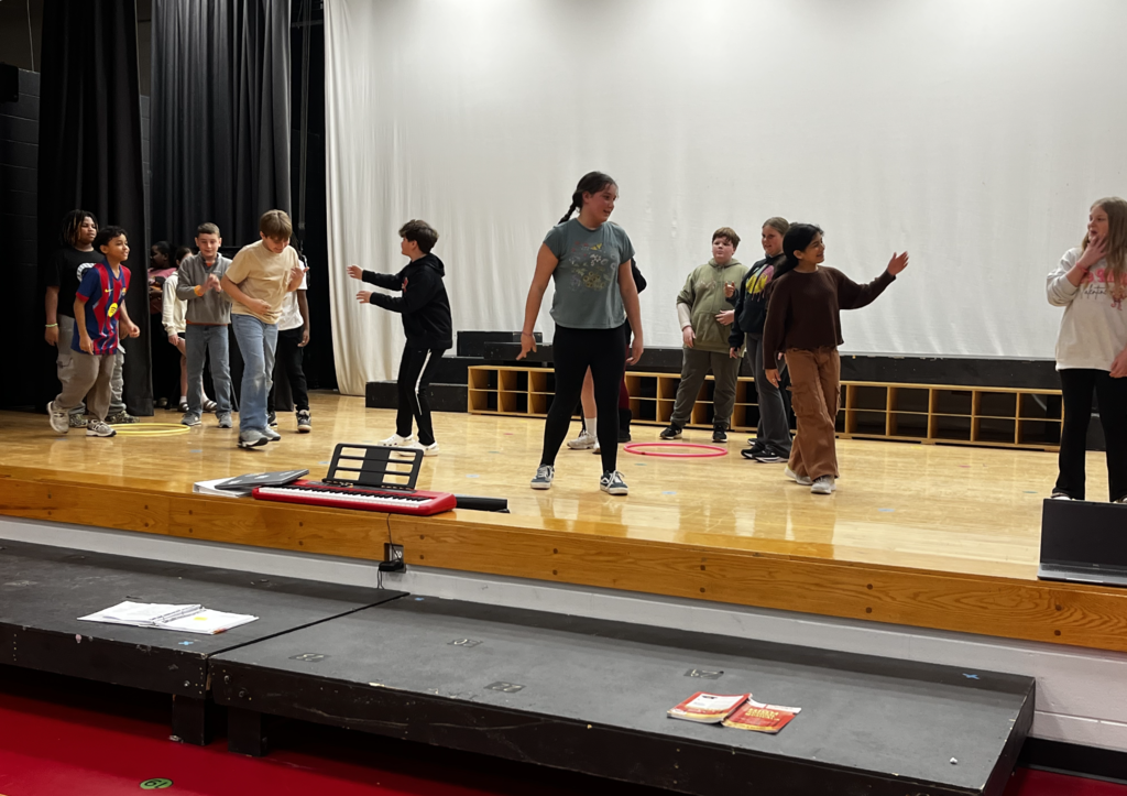 Group of students at different levels on stage, piano visible in the front