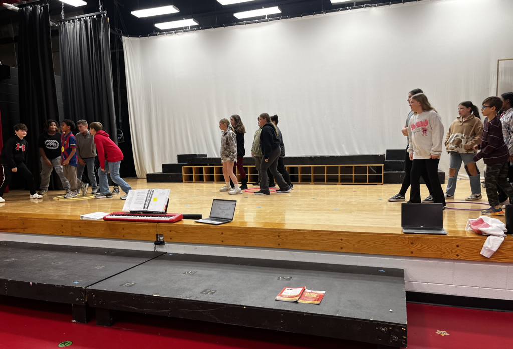 Students on stage rehearsing for musical, blocking is in clumps on each side of the stage and center