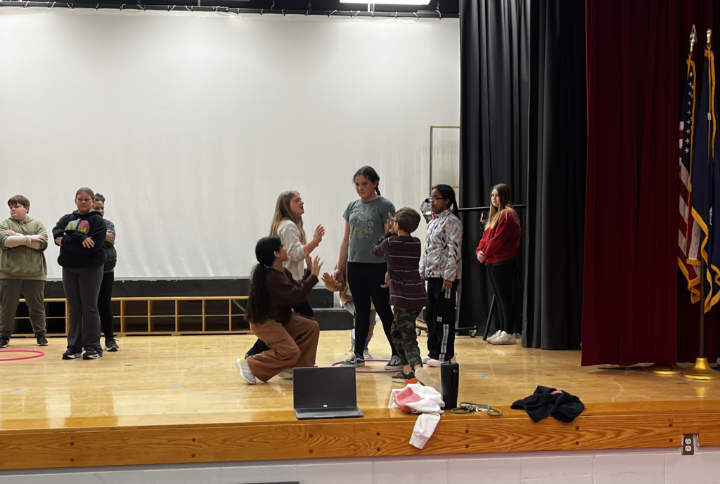 Group of students at a low level, one student standing in the middle, computer is visible in front of stage
