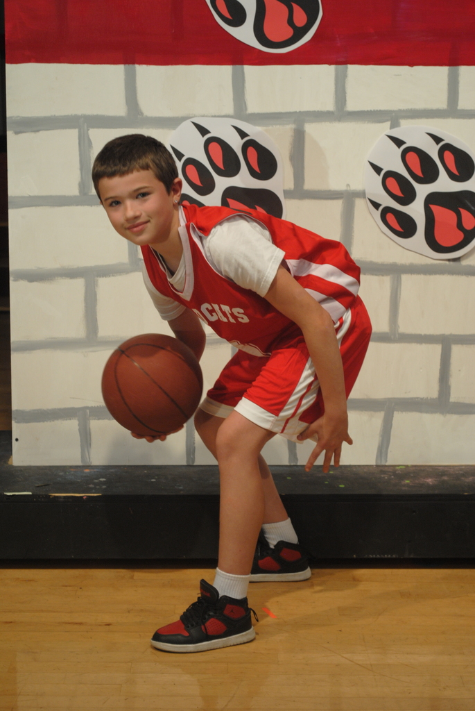 One student dressed as a basketball player dribbling the ball with a brick wall behind. 