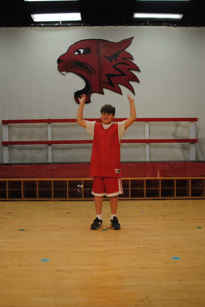 One student standing center staged wearing red and white basketball clothes with wildcat set piece in the background. 