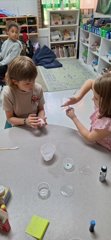 Two students holding slime sitting at their desk