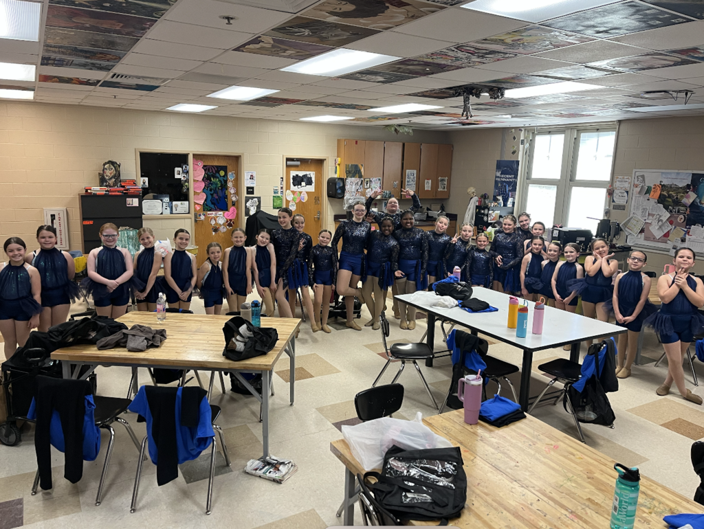 Photo features all girls wearing blue sparkly costumes smiling in a busy art room