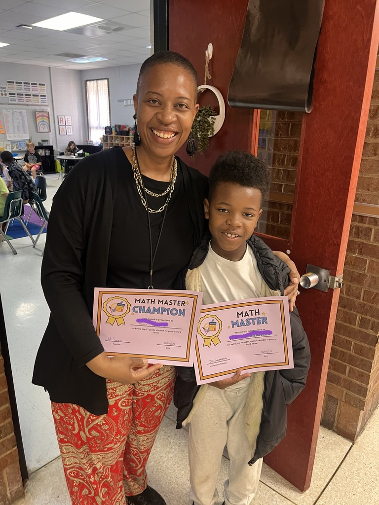 3rd grade Math Master Champion, stands with adult holding two Math Master certificates in a classroom setting.
