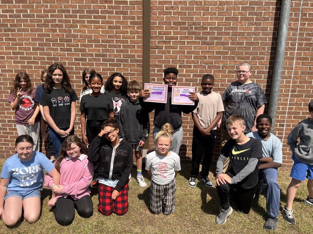 5th grade Math Master Champion, stands outdoors with classmates on grass in front of a red brick wall, holding Math Master certificates.