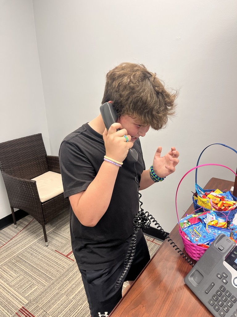 A person in a black shirt is on a phone call in an office with a basket of candies on the desk.