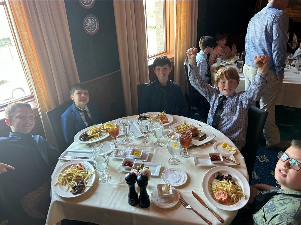 Group of children seated at a table, celebrating. A table is laden with various dishes, including fried potatoes and salads.